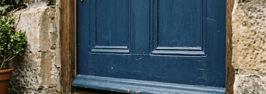 Antique brass key on stone doorstep under blue wooden door