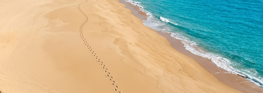 Busy sandy beach with colorful umbrellas, turquoise sea, boats, and coastal hills